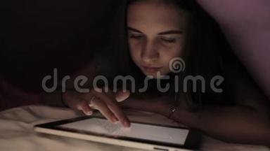 年轻女孩躲在<strong>羽绒被</strong>下，在黑暗中使用PC平板设备。 青少年晚上在数字平板电脑上玩。